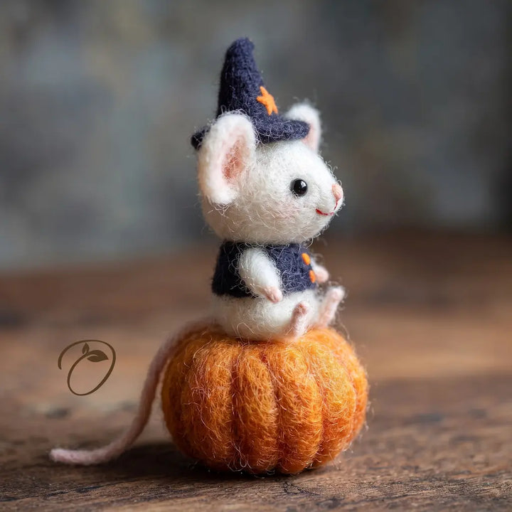 Side view of white felt mouse wearing a navy wizard hat on a pumpkin