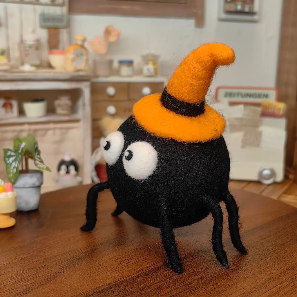 Side view of Midnight Spider wool felt figurine wearing a curved orange witch hat
