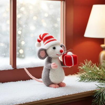 Plush toy mouse in a Santa hat holding a gift box on a snowy window ledge.