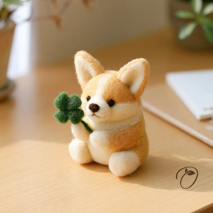 Golden tan and cream felt corgi holding a green four-leaf clover between its front paws