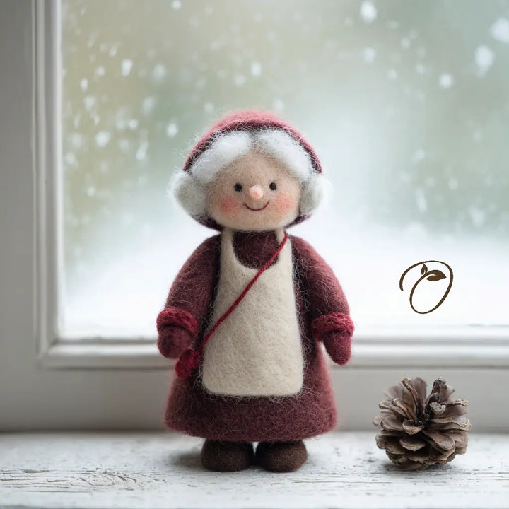 Front view of Mrs. Claus felt figurine with a burgundy bonnet, grey-white curls, cream apron, and small red crossbody bag.