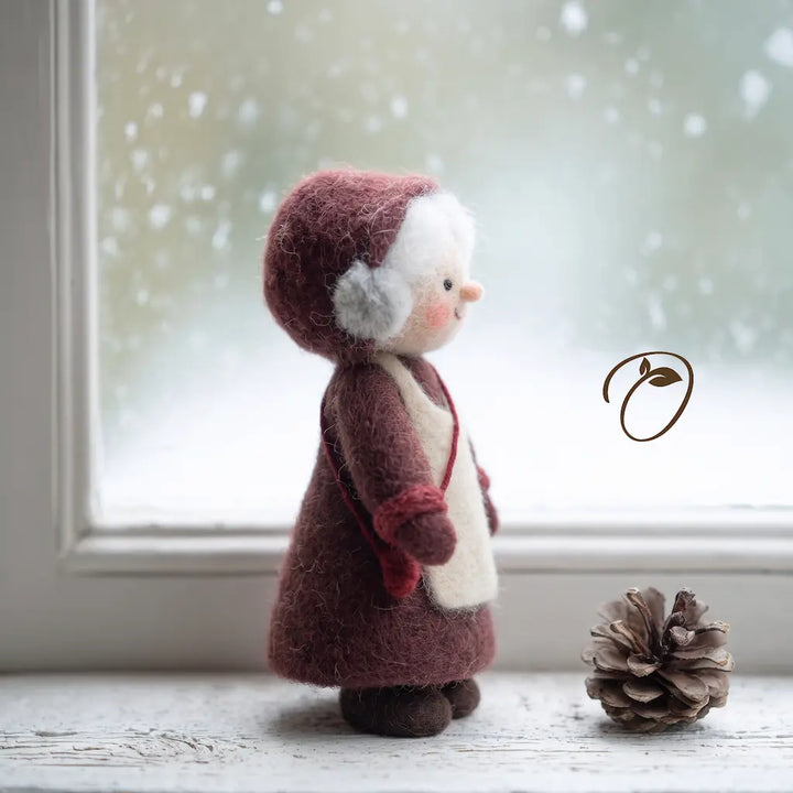Side view of Mrs. Claus felt figurine showing her rounded burgundy bonnet, cream apron, red bag, and brown shoes.