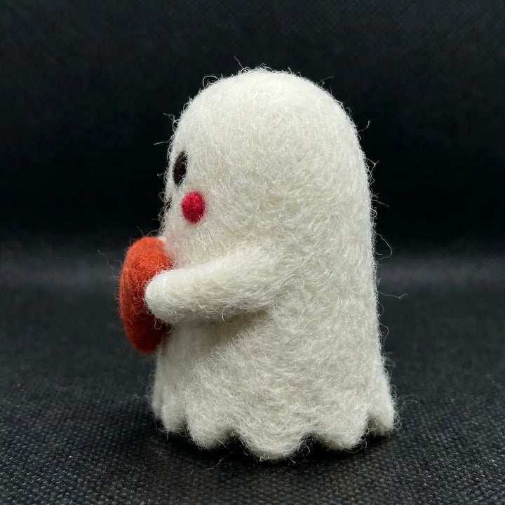 White felted ghost toy holding a red object on a dark background