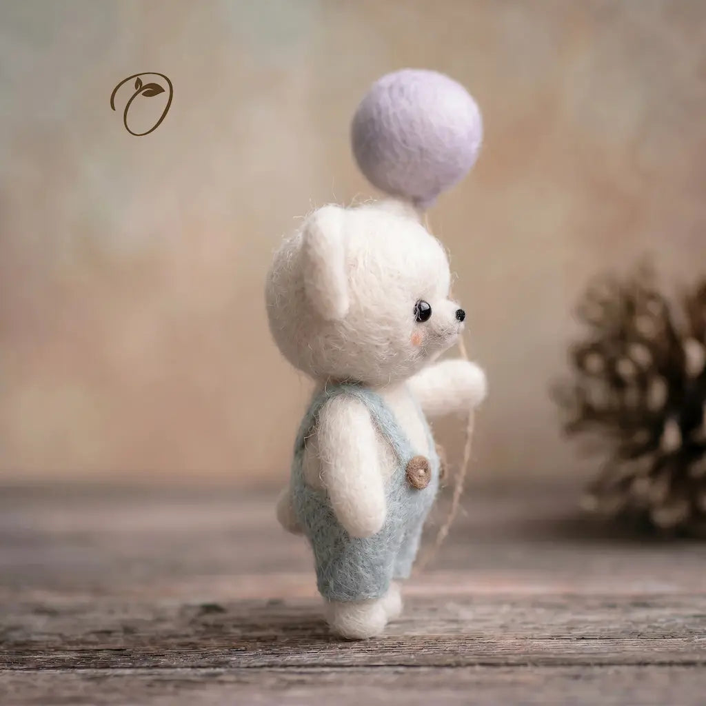 Small white teddy bear with a purple ball on its head, standing on a wooden surface with a blurred background.