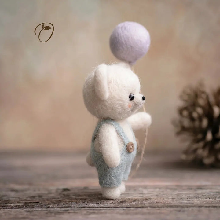 Small white teddy bear with a purple ball on its head, standing on a wooden surface with a blurred background.
