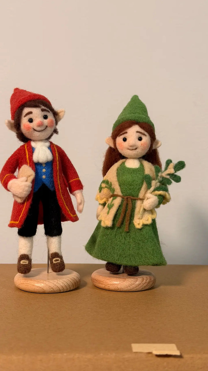 Two felted figurines, one in a red outfit and the other in a green outfit, on a plain background.