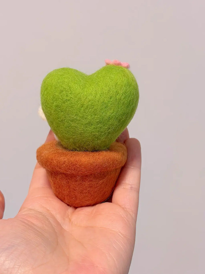 Heart-shaped green plant in a brown pot held in a hand against a plain background