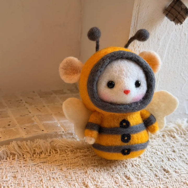 A needle-felted bee doll wearing a yellow and gray bee suit, standing on a textured cream rug in a warm indoor setting.