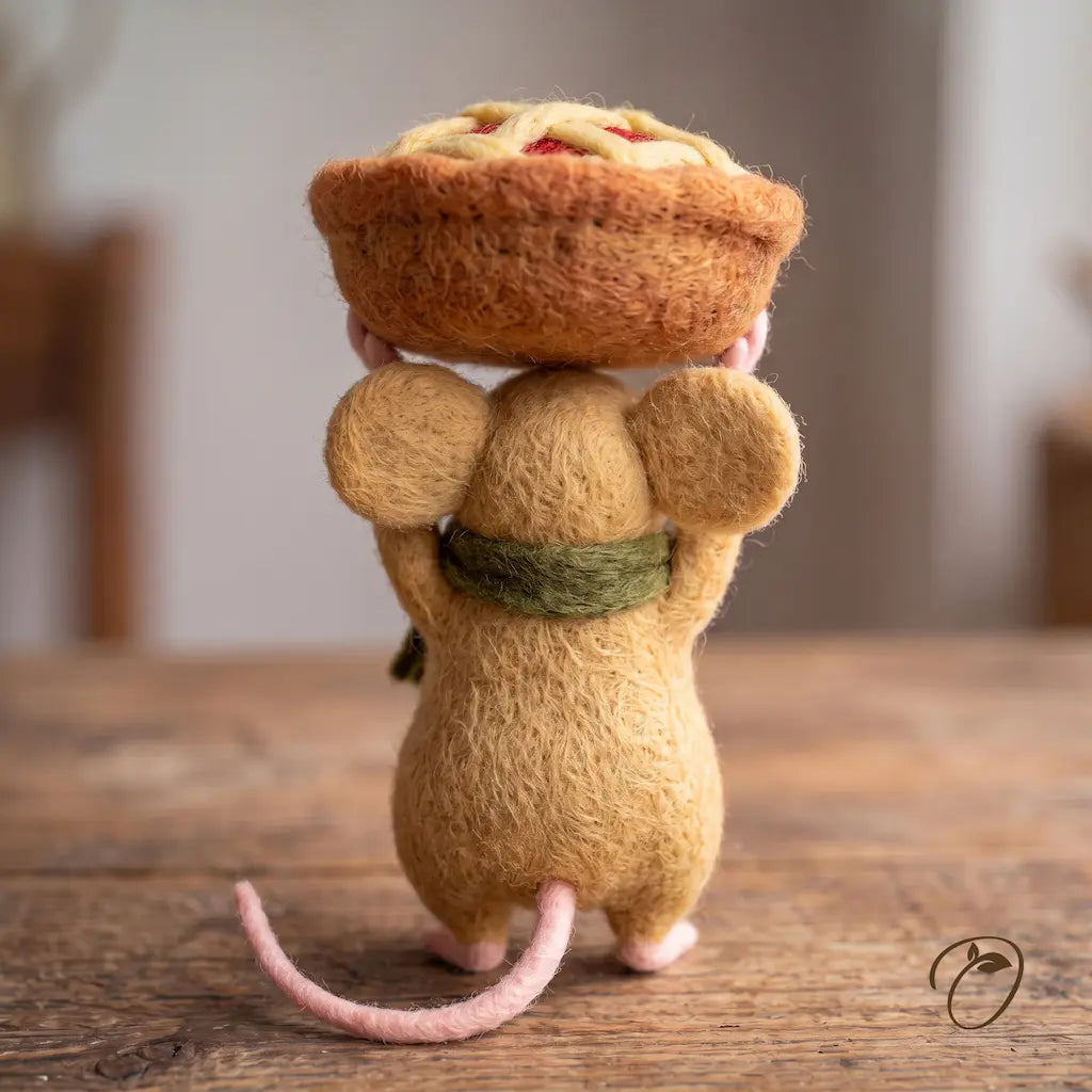 Back view of Apple Pie Parade Mouse felt figurine with rounded ears, a green scarf, a pink tail, and a pie held overhead.