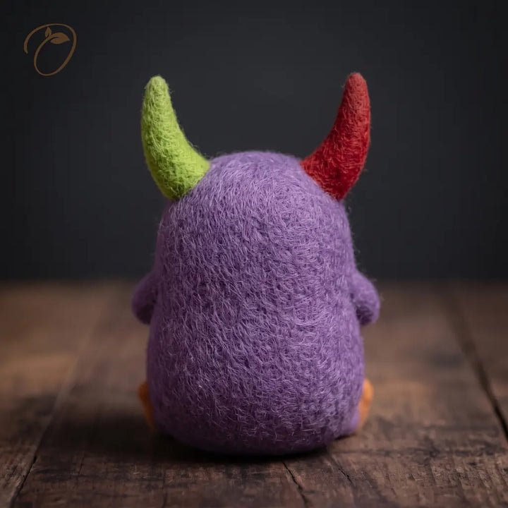 Back view of Clover Monster wool felt figurine showing its rounded purple body and red and lime-green horns