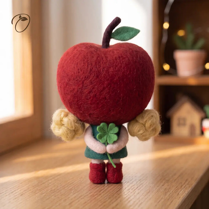 Side view of a wool felt apple girl showing the rounded red hood, apple stem and leaf, blonde curls and green dress.