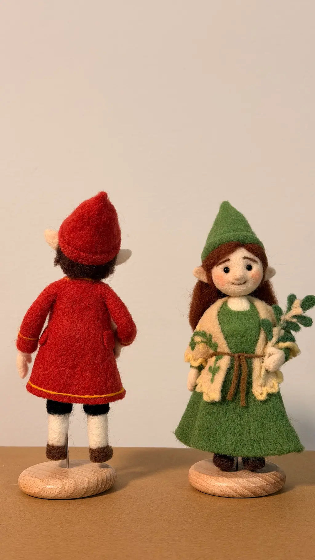 Two figurines, one in a red outfit and the other in a green outfit, standing on a brown surface with a plain background.