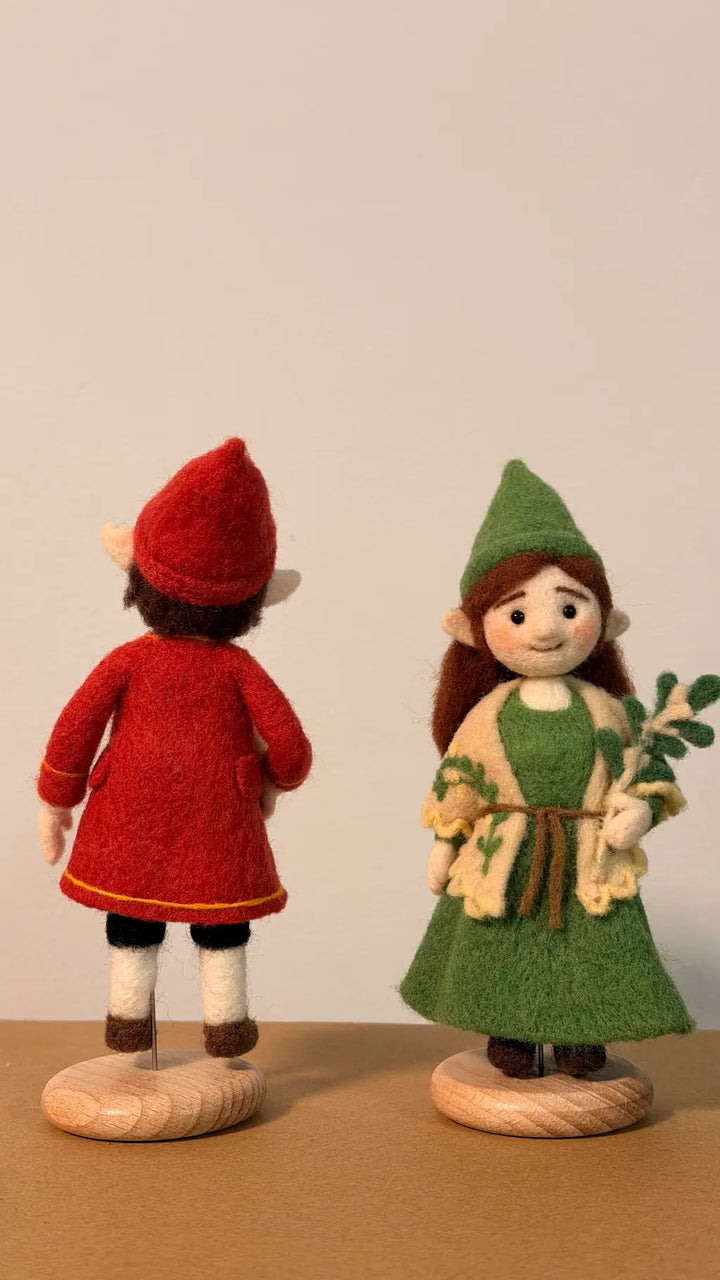 Two figurines, one in a red outfit and the other in a green outfit, standing on a brown surface with a plain background.