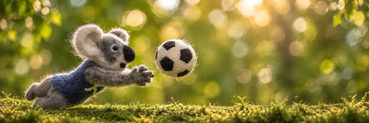 Handmade wool felt koala reaching for a soccer ball in a warm sunlit outdoor setting