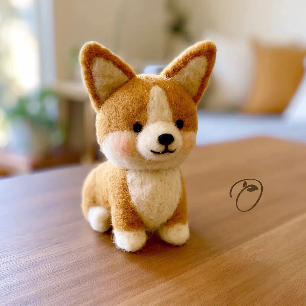 A small felt dog toy with tan and cream fur sits on a wooden table in a softly blurred indoor setting.