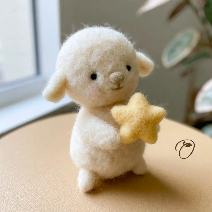 A small white wool felt lamb figurine holding a yellow star, placed on a beige surface near a window with a blurred indoor background.