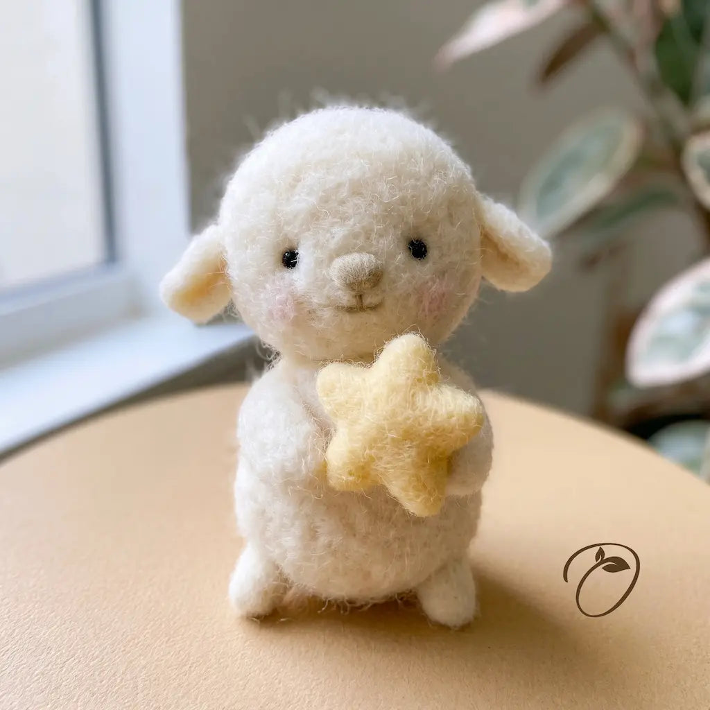 A small white felted wool lamb figurine holding a yellow star, sitting on a beige surface in a softly lit indoor setting with a window and blurred plant in the background.