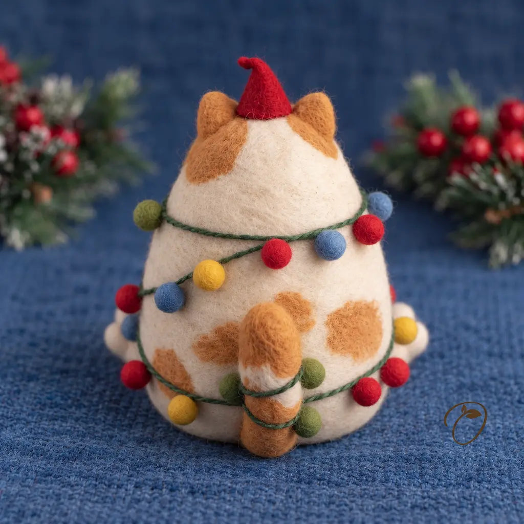 Back view of a ginger-and-cream felt cat with a red pointed hat, a striped tail and colorful baubles on green cord.