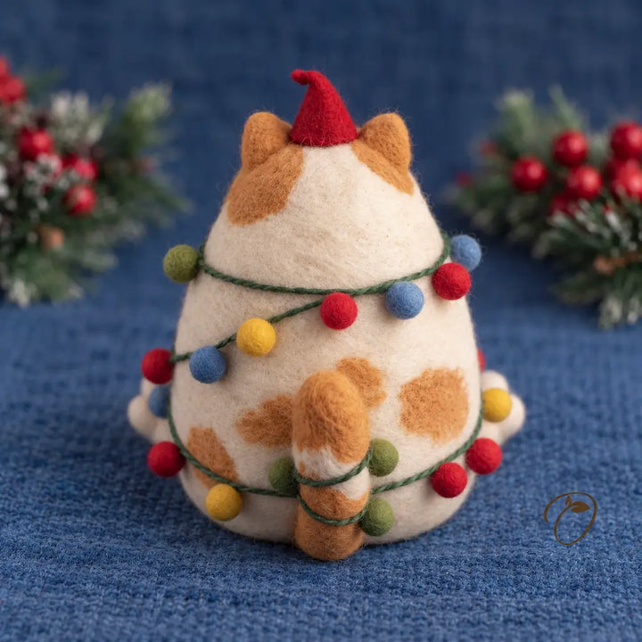 Back view of a ginger-and-cream felt cat with a red pointed hat, a striped tail and colorful baubles on green cord.