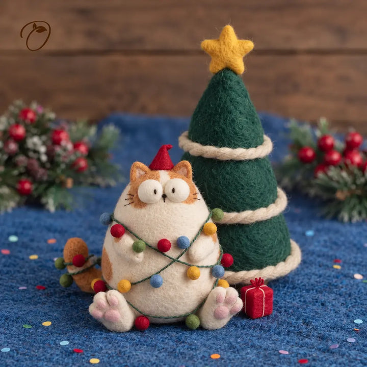 Wide-eyed ginger-and-cream felt cat in a red pointed hat and colorful bauble garland, beside a felt Christmas tree and red gift box.