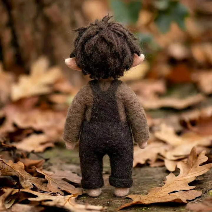 Small figurine with brown hair and clothing standing on a leaf-covered ground.