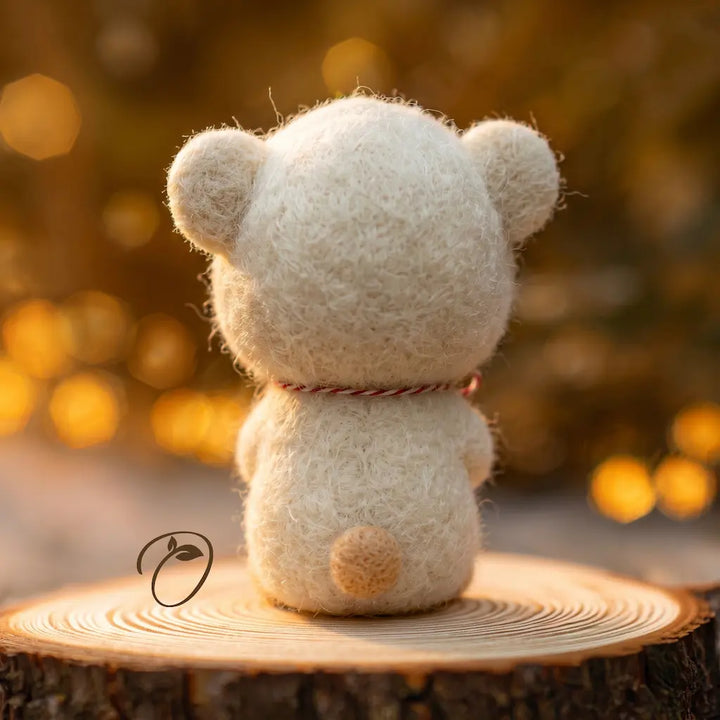 A small felt teddy bear viewed from the back, sitting on a round tree stump with a warm golden bokeh background.