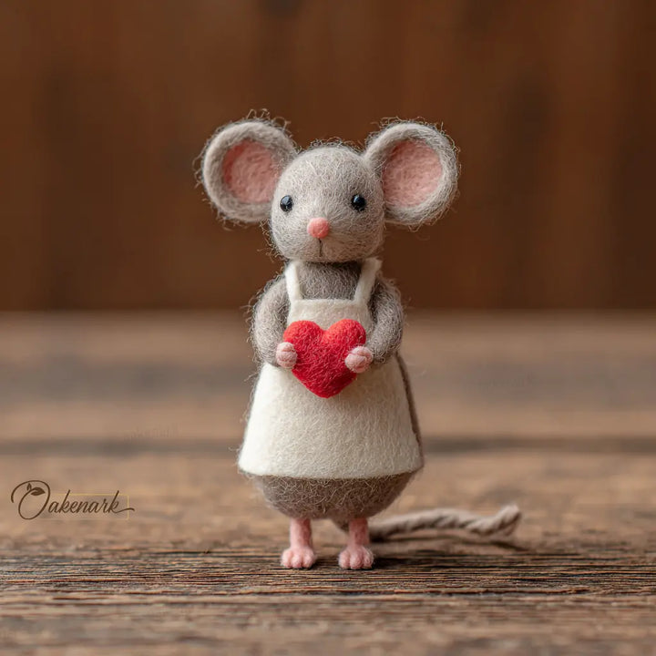 Felted mouse toy holding a red heart on a wooden surface with &
