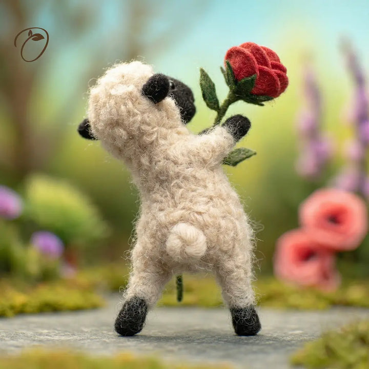 Toy sheep holding a red flower in a garden setting