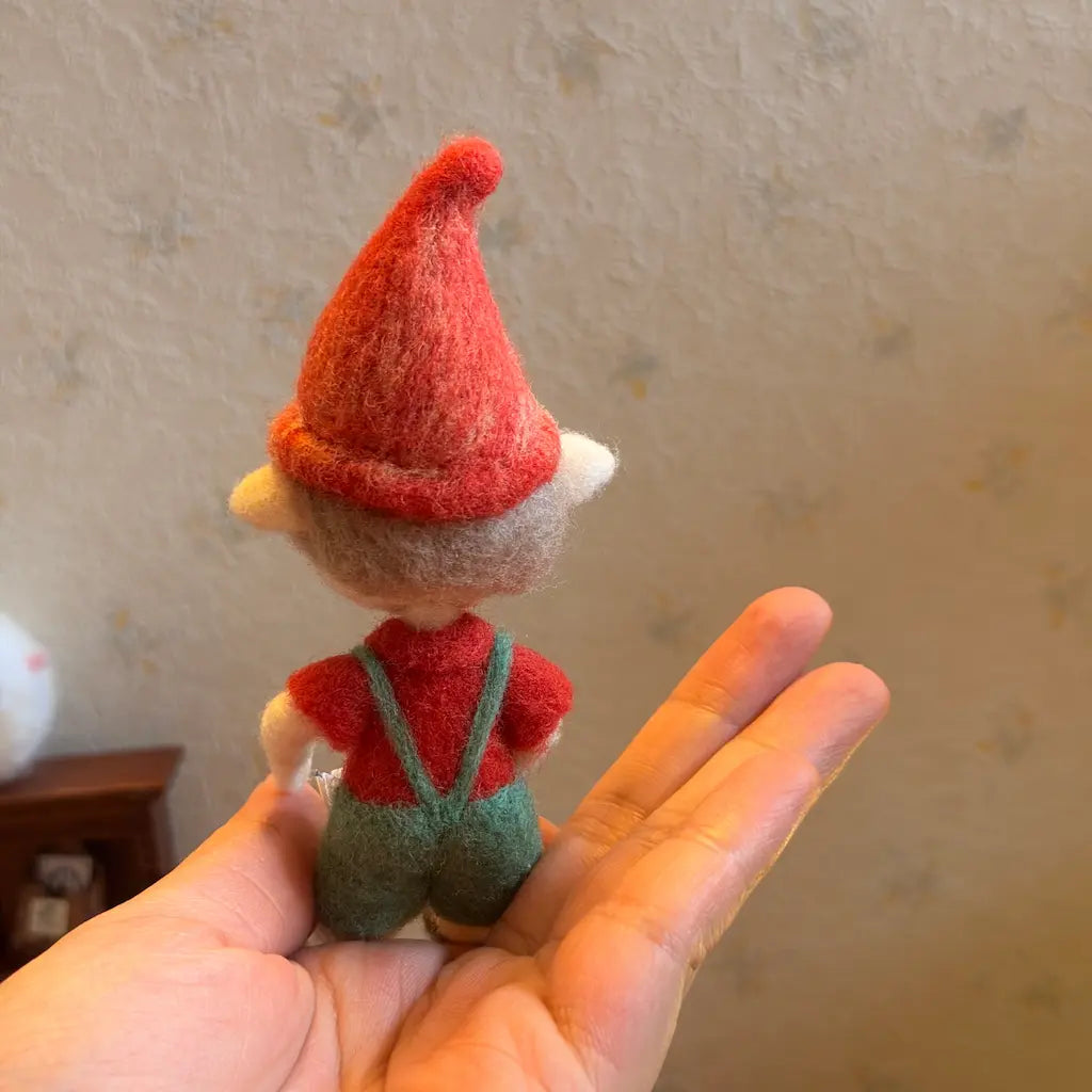 Small felt elf toy held in a hand against a neutral background