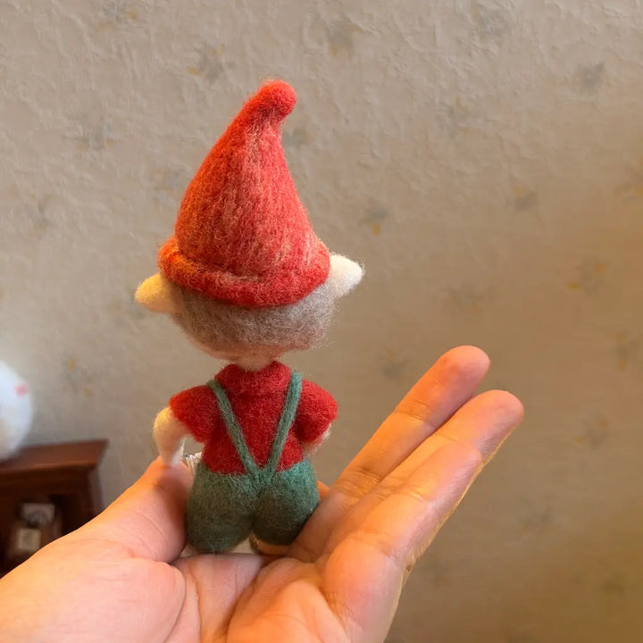 Small felt elf toy held in a hand against a neutral background
