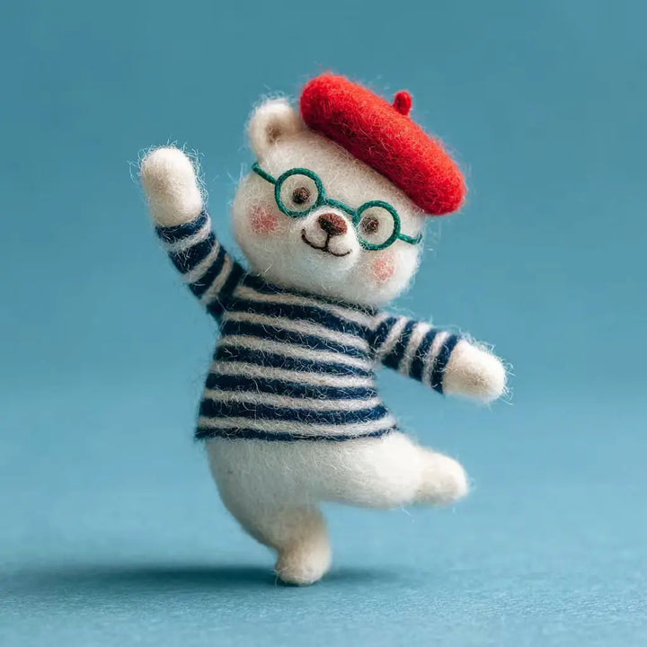 Felted toy of a white animal wearing a red beret and striped sweater on a blue background