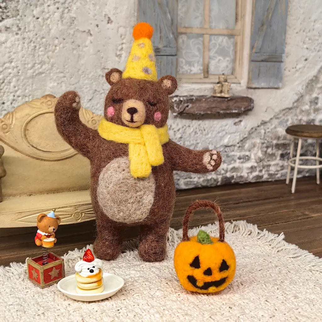 Party Bear felt figurine wearing a yellow party hat and scarf beside a jack-o-lantern basket and miniature cake