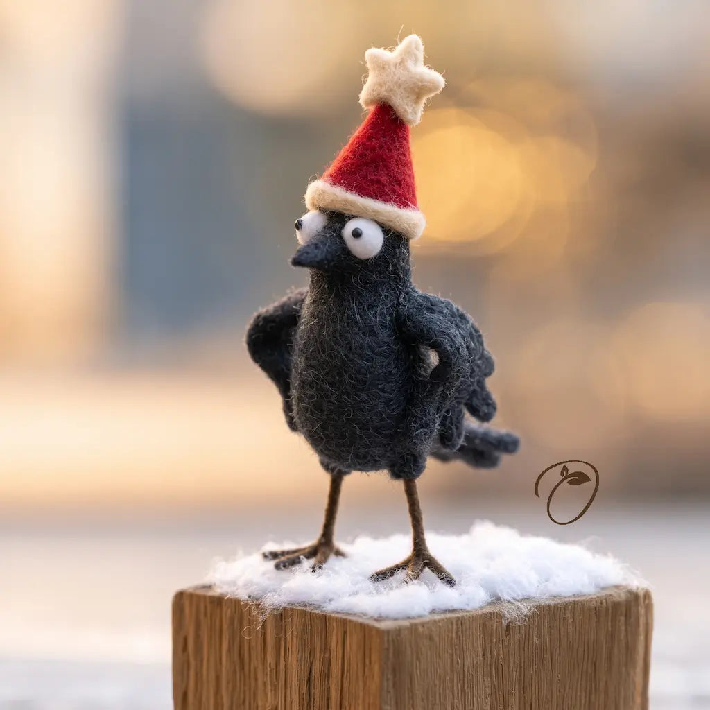 Three-quarter view of a charcoal felt crow with wings on its hips and a red Christmas hat topped with a cream star.