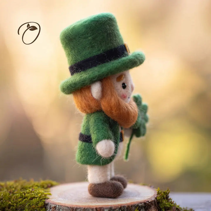 Side view of a wool felt leprechaun showing the green top hat, orange beard, green coat, cream trousers and brown shoes.