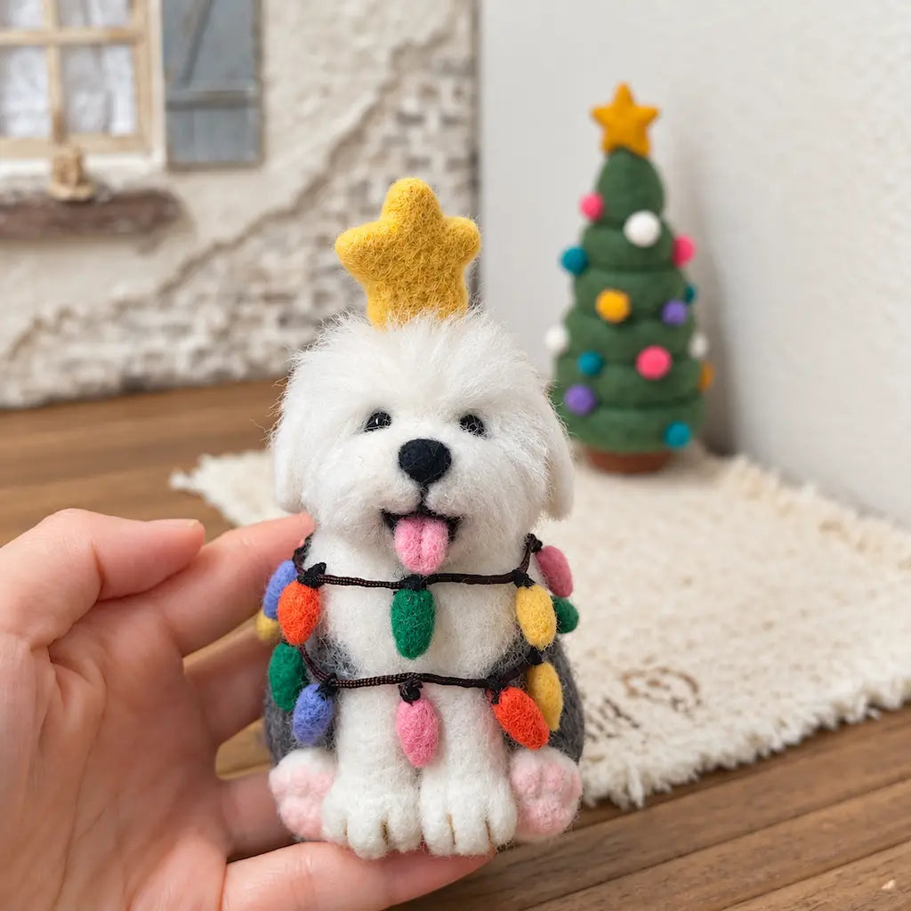 Hand-held Old English Sheepdog wool felt figurine with a golden star and colorful bulb garlands, with a miniature tree behind.