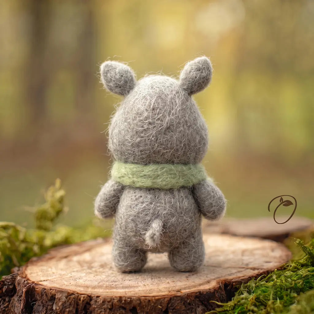 Back view of a gray wool felt rhino with rounded ears, a green scarf around its neck and a short tufted tail.