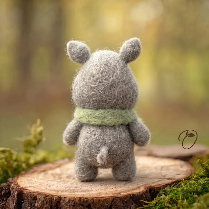 Back view of a gray wool felt rhino with rounded ears, a green scarf around its neck and a short tufted tail.