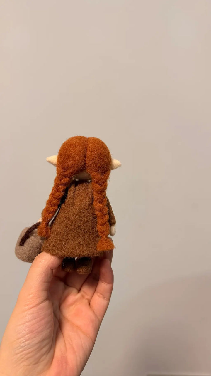Small brown plush toy held in a hand against a plain background