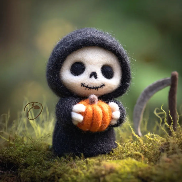 A small felted needle art figurine of a skeleton in a black hood holding an orange pumpkin, standing on mossy ground with a blurred natural background.