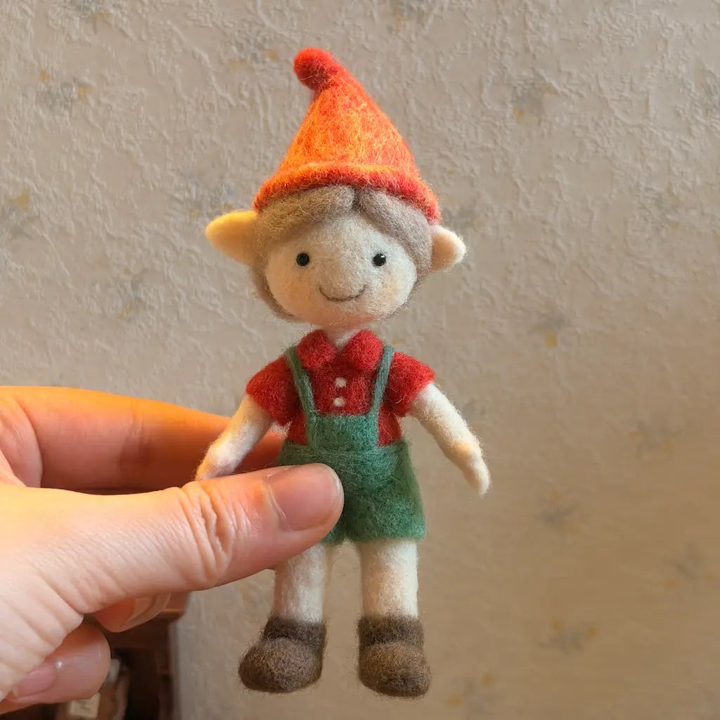 Small toy figure with a red hat and green overalls held by a hand against a neutral background