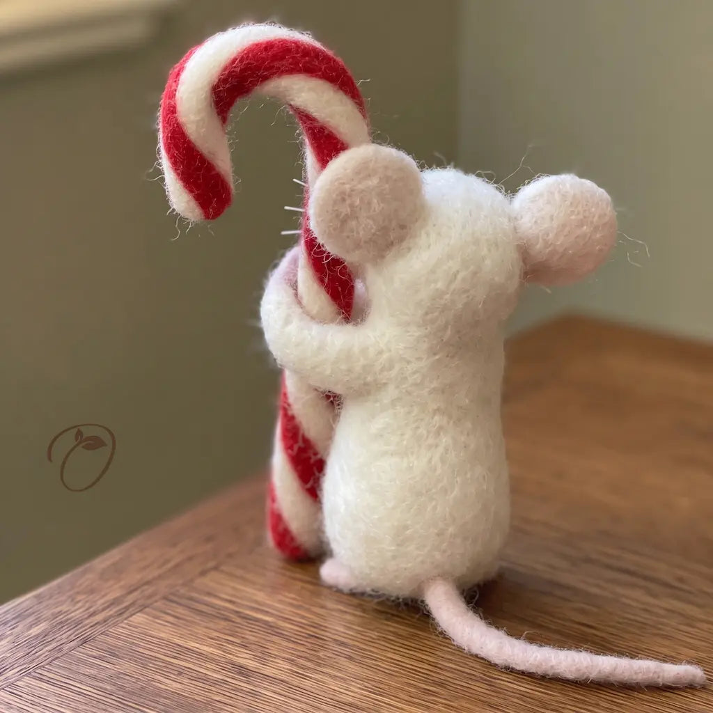 Back view of an ivory wool felt mouse hugging a candy cane, with rounded ears and a long pale pink tail.