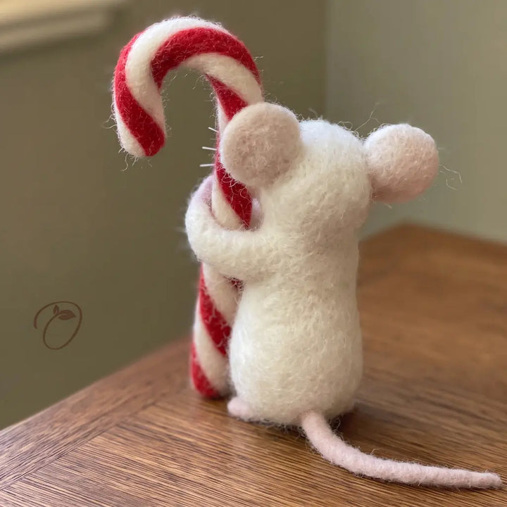 Back view of an ivory wool felt mouse hugging a candy cane, with rounded ears and a long pale pink tail.