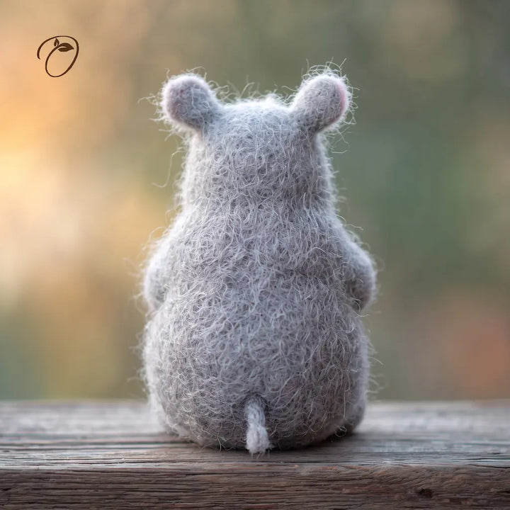 Back view of a seated gray felt rhino with rounded ears, a short tail and visible wool fibers on a wooden surface.