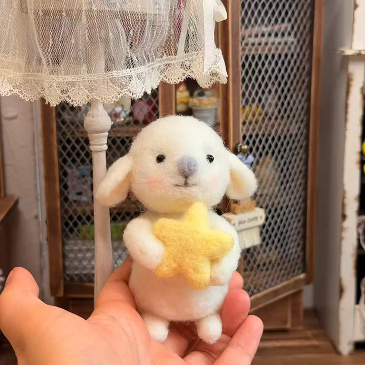 A small white felt lamb plush toy with a yellow star held in its front paws, being held in a person&