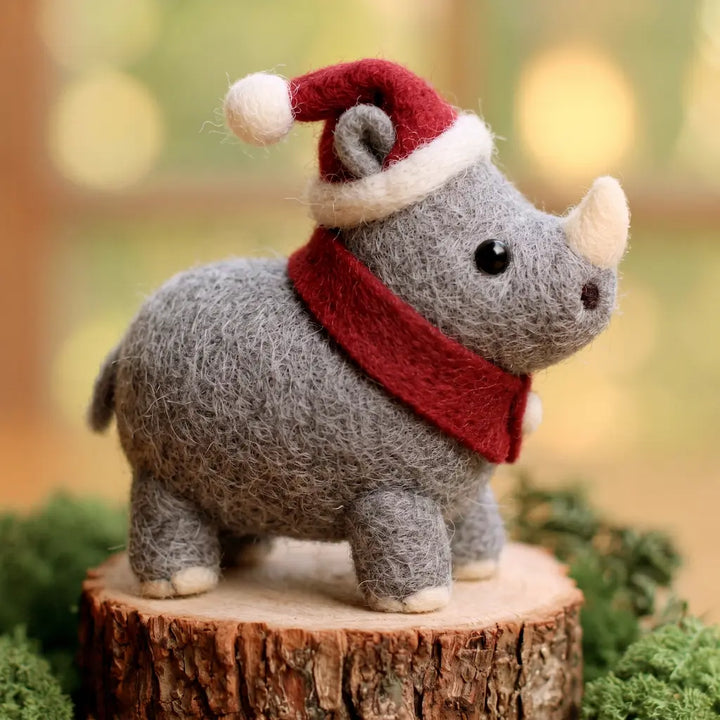 Side view of a gray felt rhino with a cream-colored horn, red Santa hat and scarf, rounded body and short tail.