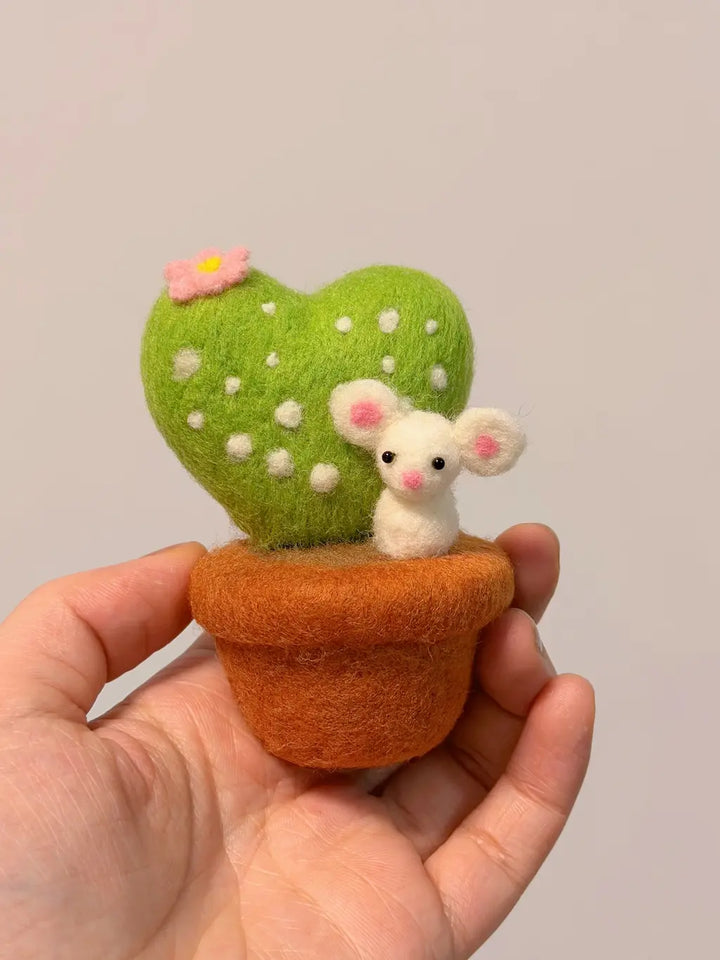 Small felt mouse and heart-shaped plant in a pot held in a hand against a plain background