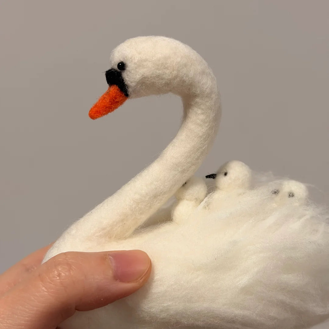 White swan plush toy with orange beak held by a hand against a gray background