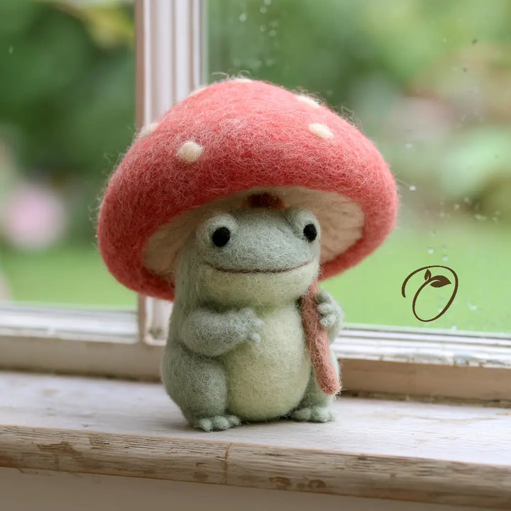 Sage green felt frog holding a pink mushroom umbrella with cream spots, shown from the front