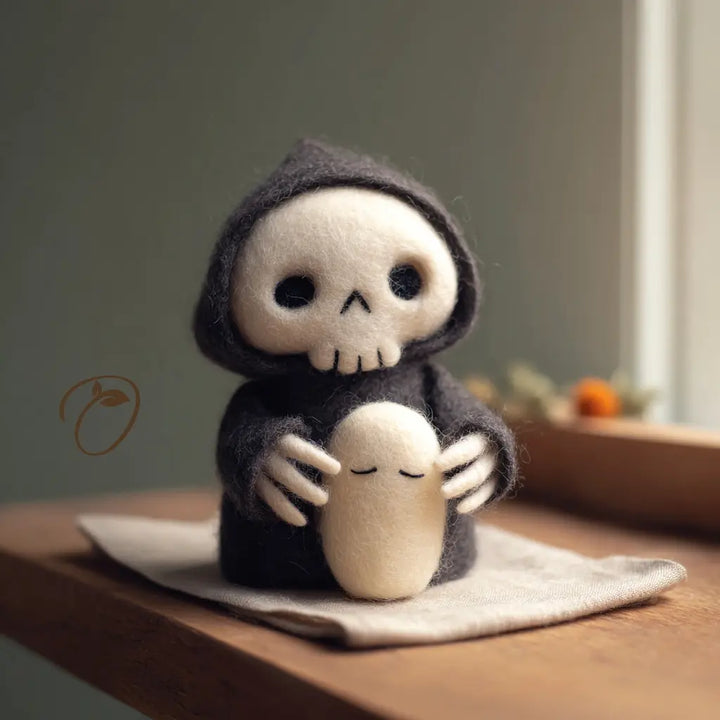 Charcoal-hooded felt reaper with an ivory skull face gently holding a small ivory ghost with closed eyes.