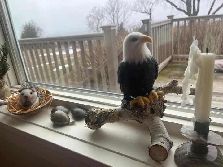 Model of a bald eagle on a branch with a small animal figurine and candles on a windowsill.